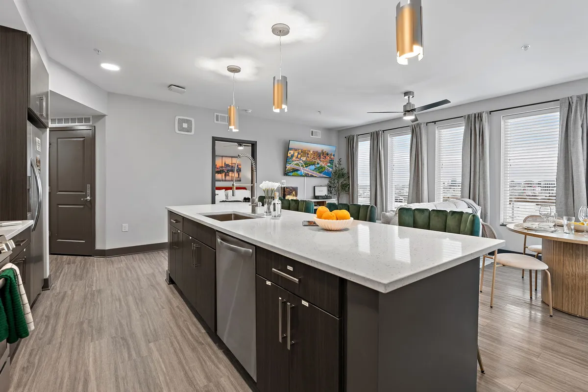 This image features a stylish kitchen island, modern appliances, large windows that allow plenty of natural light, and a dining table nearby. The space looks sleek and contemporary, with a functional layout perfect for both casual cooking and entertaining guests.