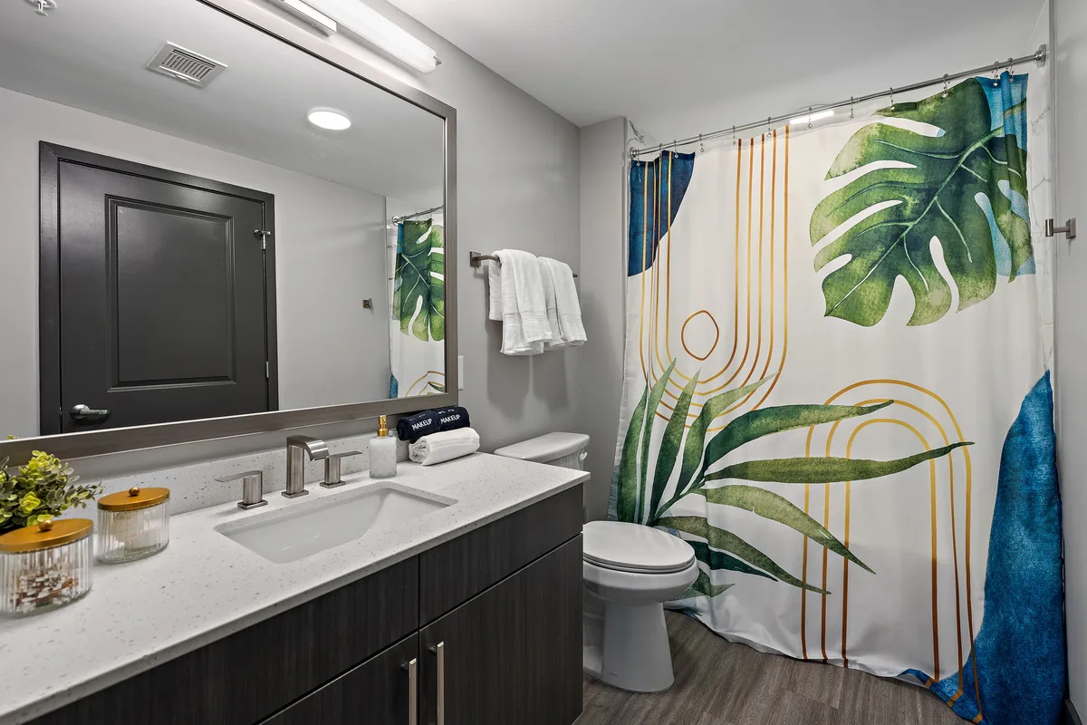 A vibrant bathroom scene with a large mirror, colorful shower curtain, and modern vanity fixtures. The space feels fresh and inviting, ideal for both quick morning routines and longer, relaxing moments.
