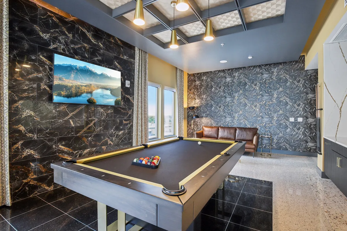 This image features a pool table as the main focal point, complemented by a large screen TV and a leather sofa along a decorative wall. The space is designed for entertainment, socializing, and relaxation, offering a luxurious yet inviting atmosphere for group activities.
