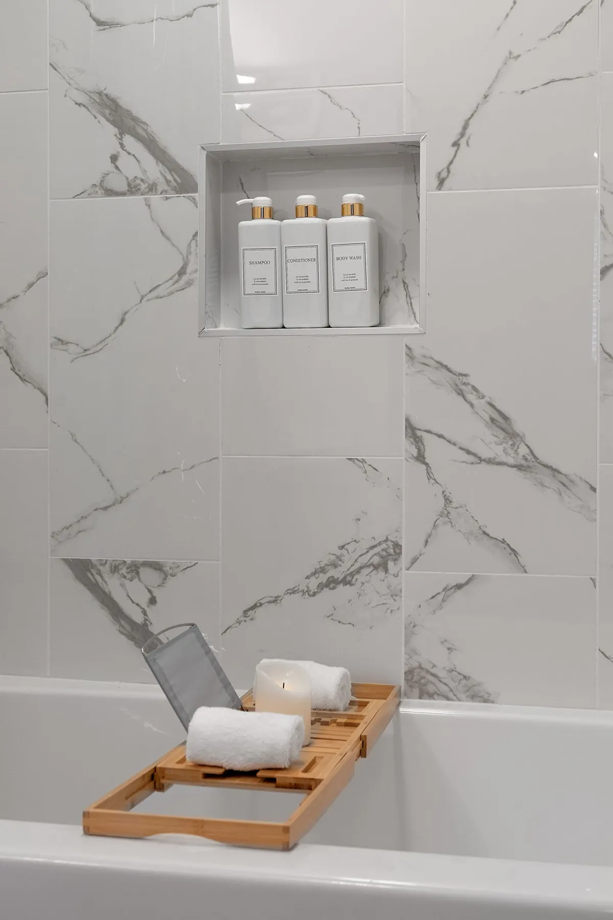 A modern bathroom featuring marble-patterned tiles, a shelf with toiletries, and a bath tray adorned with candles and towels. The atmosphere is spa-like, evoking luxury and self-care. Every element invites relaxation and rejuvenation after a busy day.