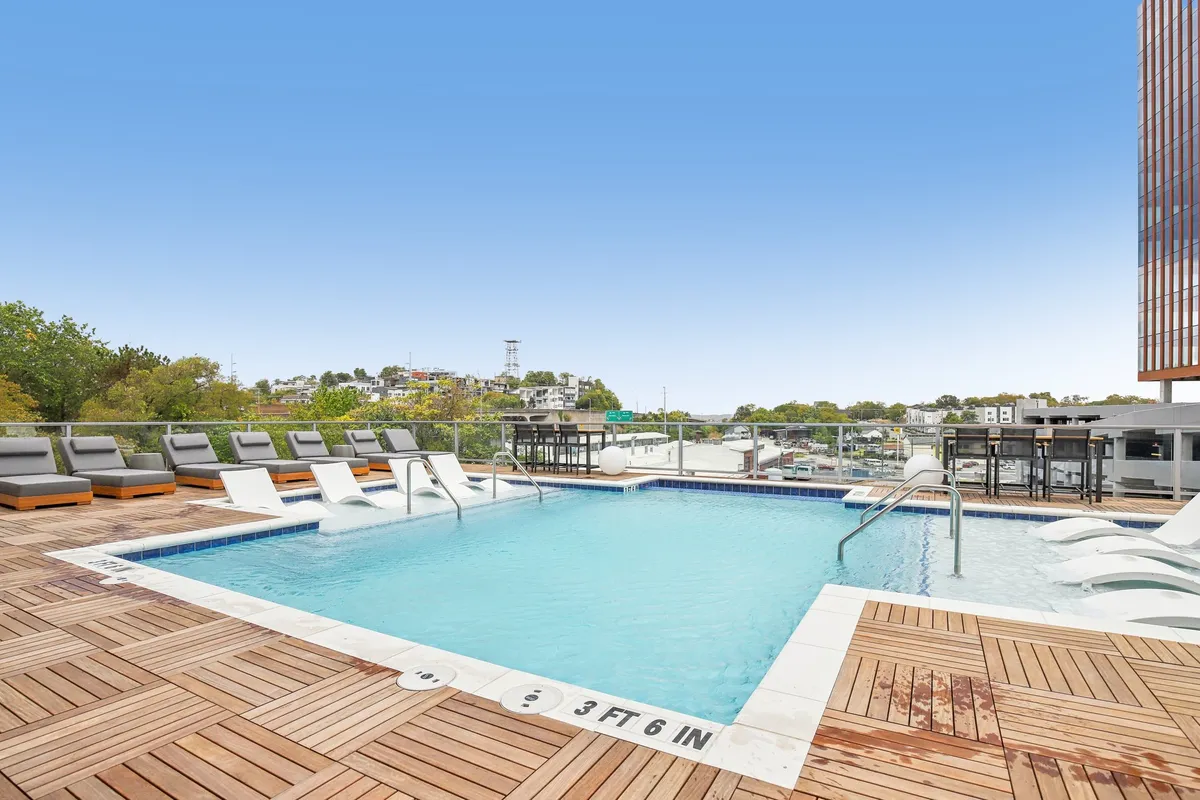 This exterior shot showcases a stylish swimming pool area with a wooden deck, inviting lounge chairs, and a stunning view of the Nashville city skyline beyond. The setting is bright and lively, with the cityscape providing a distinct sense of place and connection to Nashville’s urban energy.
